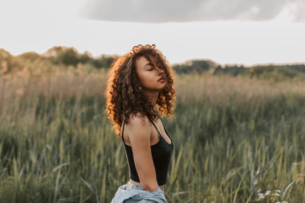 Beautiful woman with curly hair enjoying a summer day in a green field.